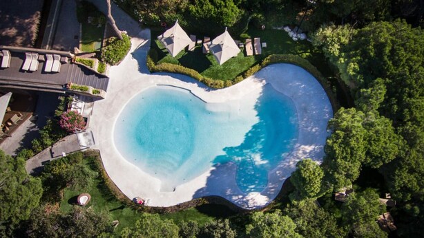 An aerial view of a property with a large circular swimming pool surrounded by lush greenery and a few buildings. - Apartment mit Pool in Strandnähe (Castiglione della Pescaia)