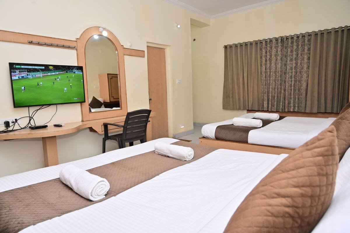 Quarto de hotel com duas camas, uma mesa de trabalho com televisão, um espelho e uma janela com cortinas.