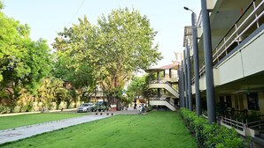 A courtyard with a green lawn, a pathway, and a building with a staircase and columns. - SWAMY RESORT (Shirdi)
