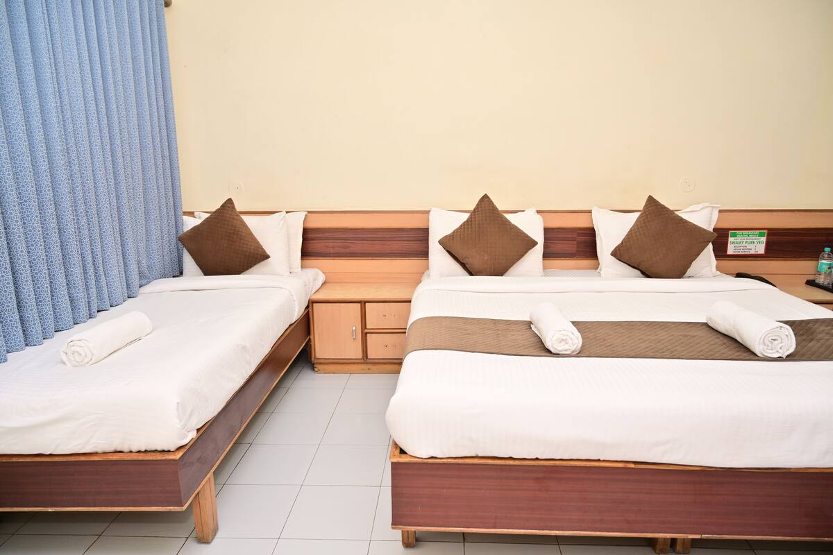Quarto de hotel com duas camas, cabeceiras de madeira, lençóis brancos, almofadas castanhas, mesa de cabeceira de madeira e um aviso indicando opções vegetarianas.