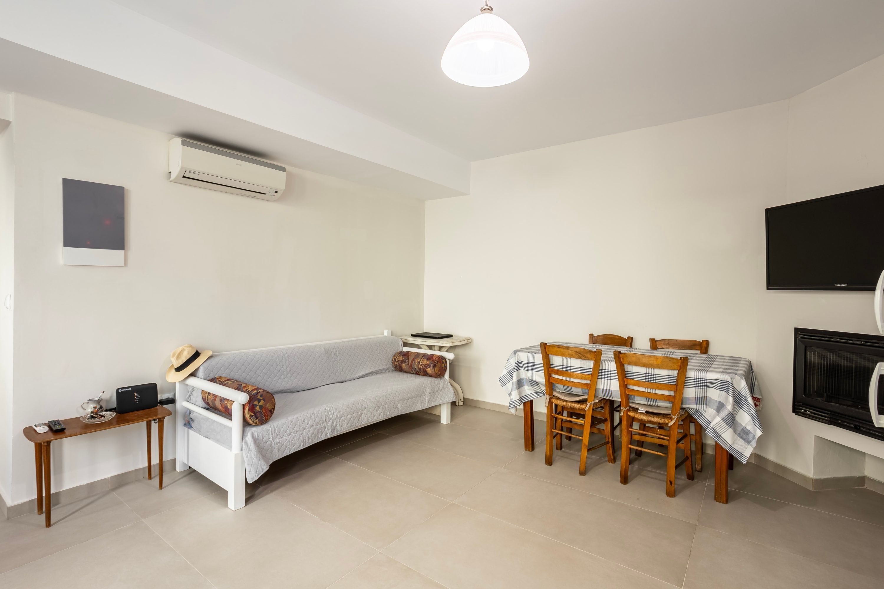 A living room with a sofa, dining table, chairs, a TV, and an air conditioning unit.