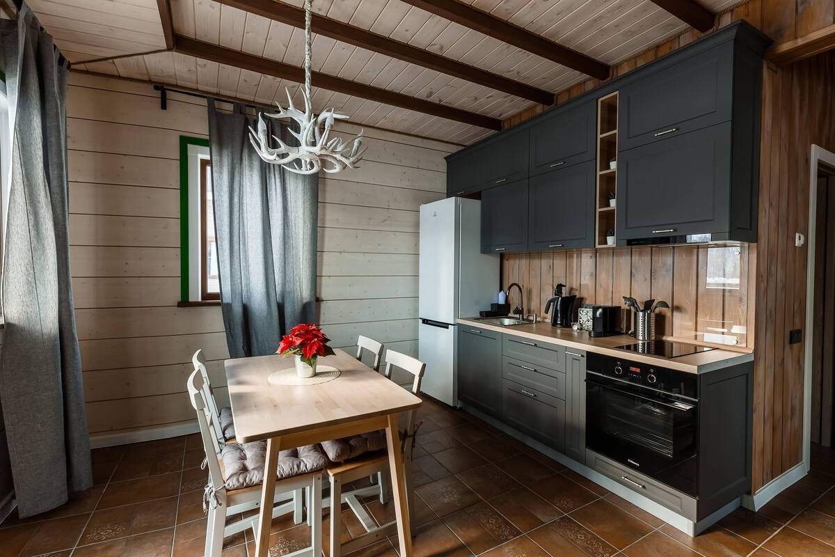 Una cocina moderna con armarios oscuros, horno empotrado y un comedor con mesa y sillas de madera.