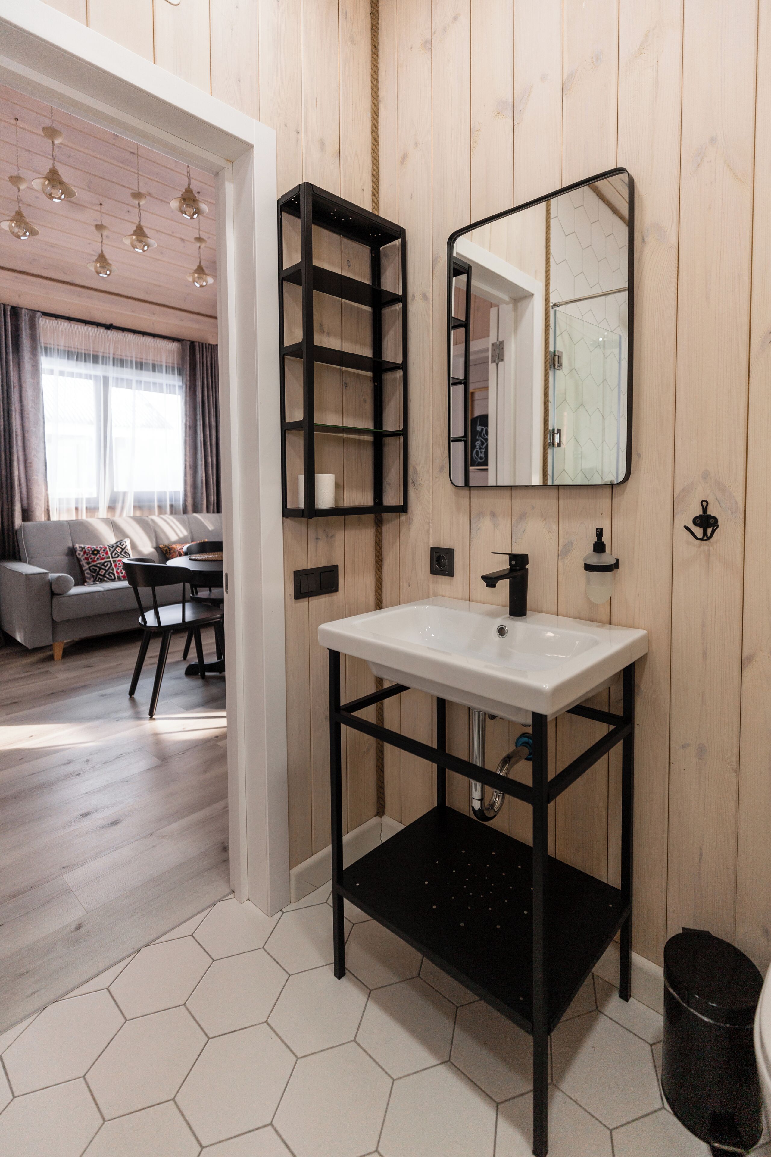 A modern bathroom with a white sink, black shelving, and a mirror.