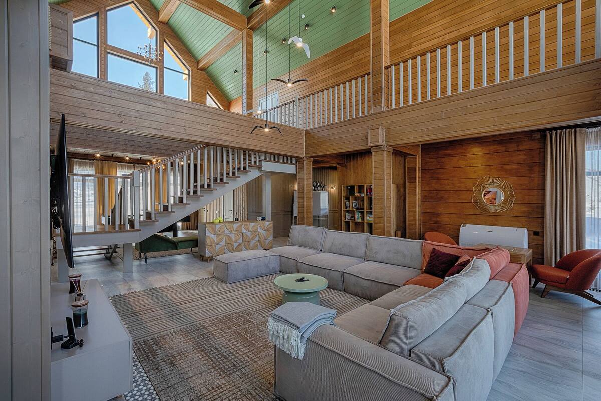 Amplia sala de estar con un sofá modular grande, una escalera y techo de madera.