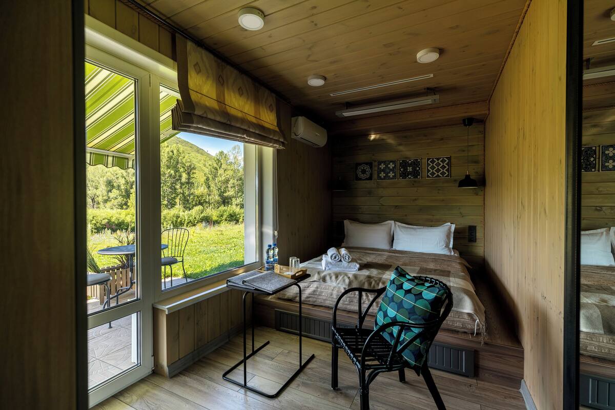 Una habitación acogedora con cama, una silla, una mesita y ventana con vistas a un jardín.