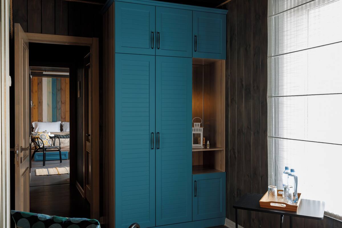 Habitación con un armario azul turquesa, una cama con almohada estampada y una mesita con botellas de agua.
