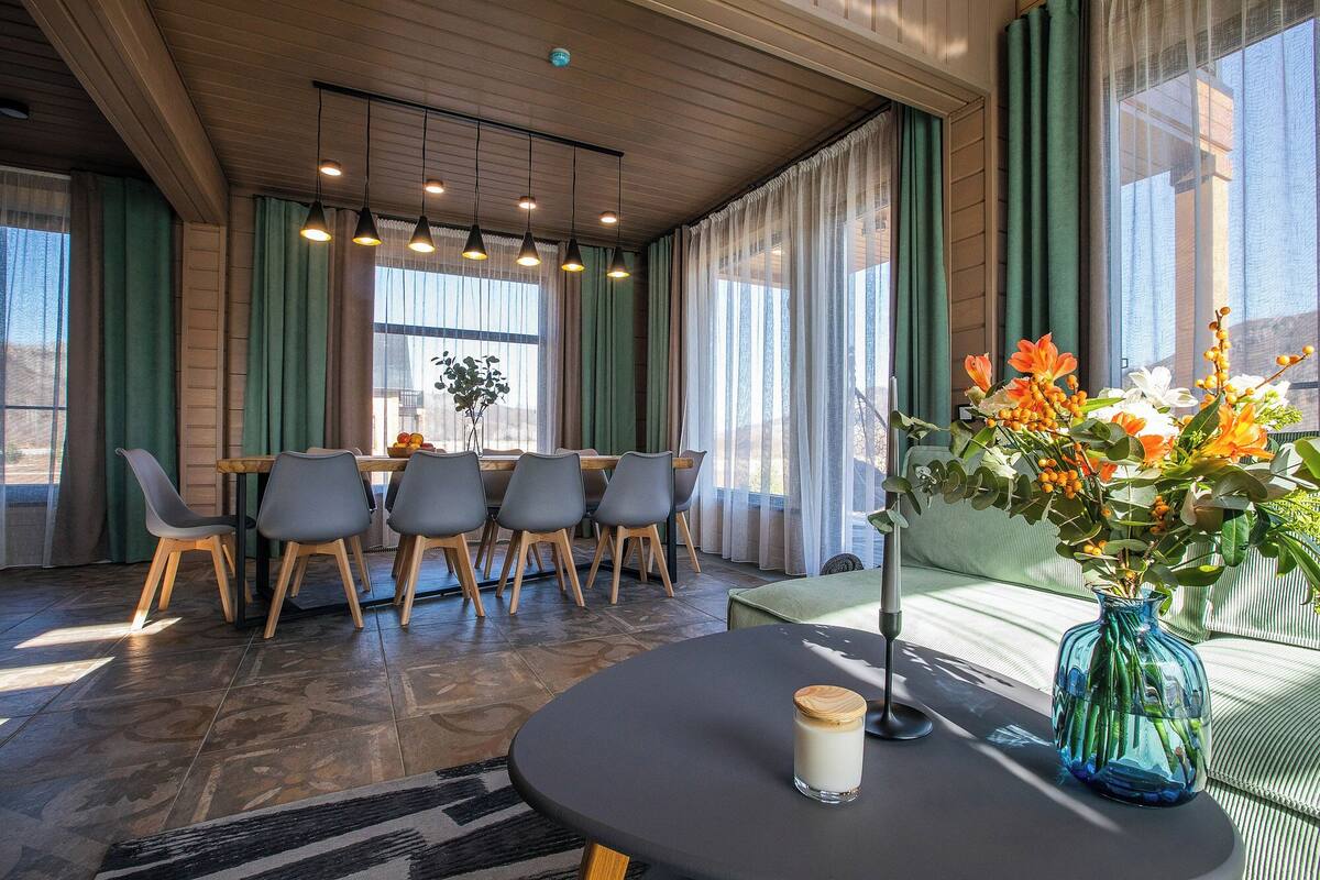 Un comedor con una mesa y sillas de madera, un jarrón con flores y una vela sobre la mesa.