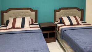 A room with two beds, each with a striped pillow and a blue bedspread. There is a small wooden nightstand between the beds, and a painting of horses on the wall. - Hotel O Depok near Bhayangkara BRIMOB Hospital Formerly Hotel Mutiara Kelapa Dua Depok (Depok)