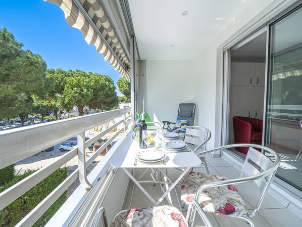A balcony with a table set for dining, a chair, and a red sofa.