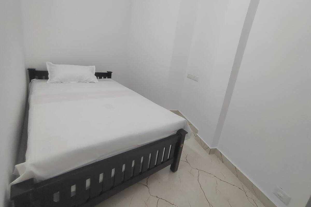 A small, single-bed room with white walls and a simple wooden bed frame.