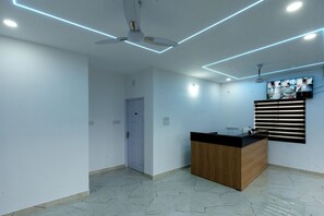 Un espace d’accueil moderne avec un comptoir en bois, des ventilateurs de plafond, un éclairage encastré et un téléviseur fixé au mur.