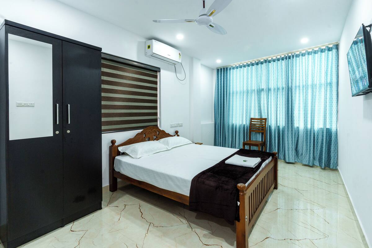 A bedroom with a bed, wardrobe, ceiling fan, air conditioning unit, and a TV.