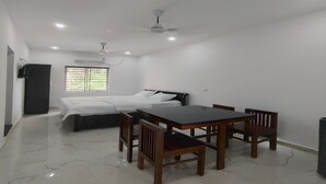 Quarto com cama, mesa, cadeiras, ventilador de teto e janela com persianas.