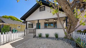 Une maison à deux étages, à l’extérieur blanc, avec un toit foncé et un petit porche agrémenté d’une clôture en bois peinte en blanc.