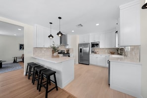 A modern kitchen with white cabinetry, a central island with stools, stainless steel appliances, and pendant lighting.