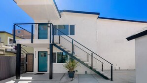 A modern two-story house with a visible staircase, a potted plant, and a clear blue sky.