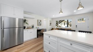 A modern kitchen with a stainless steel refrigerator, white cabinetry, a large island with a white countertop, and pendant lighting.