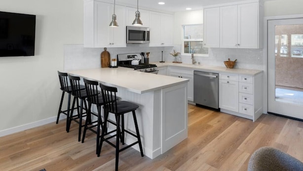 A modern kitchen with white cabinetry, a central island with bar stools, a microwave, stove, and dishwasher.