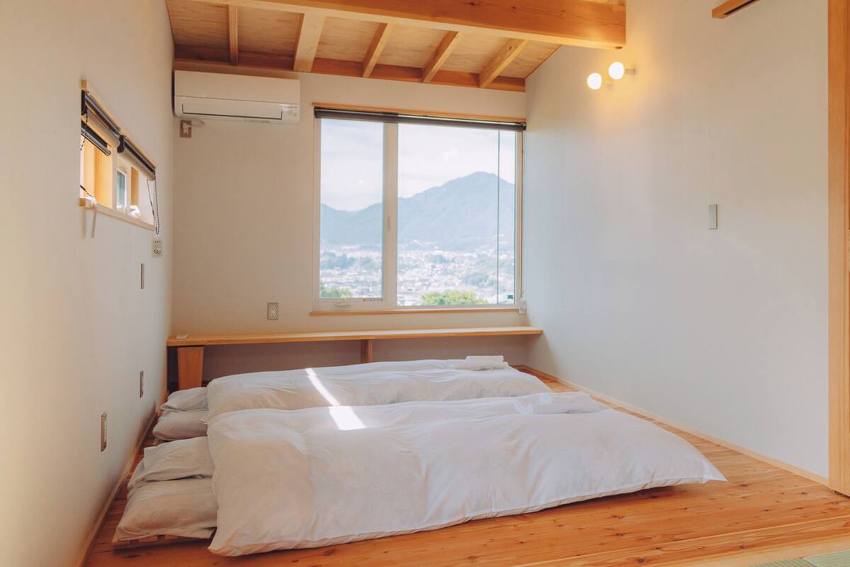 A bedroom with a large window, wooden beams, and a bed with white bedding.