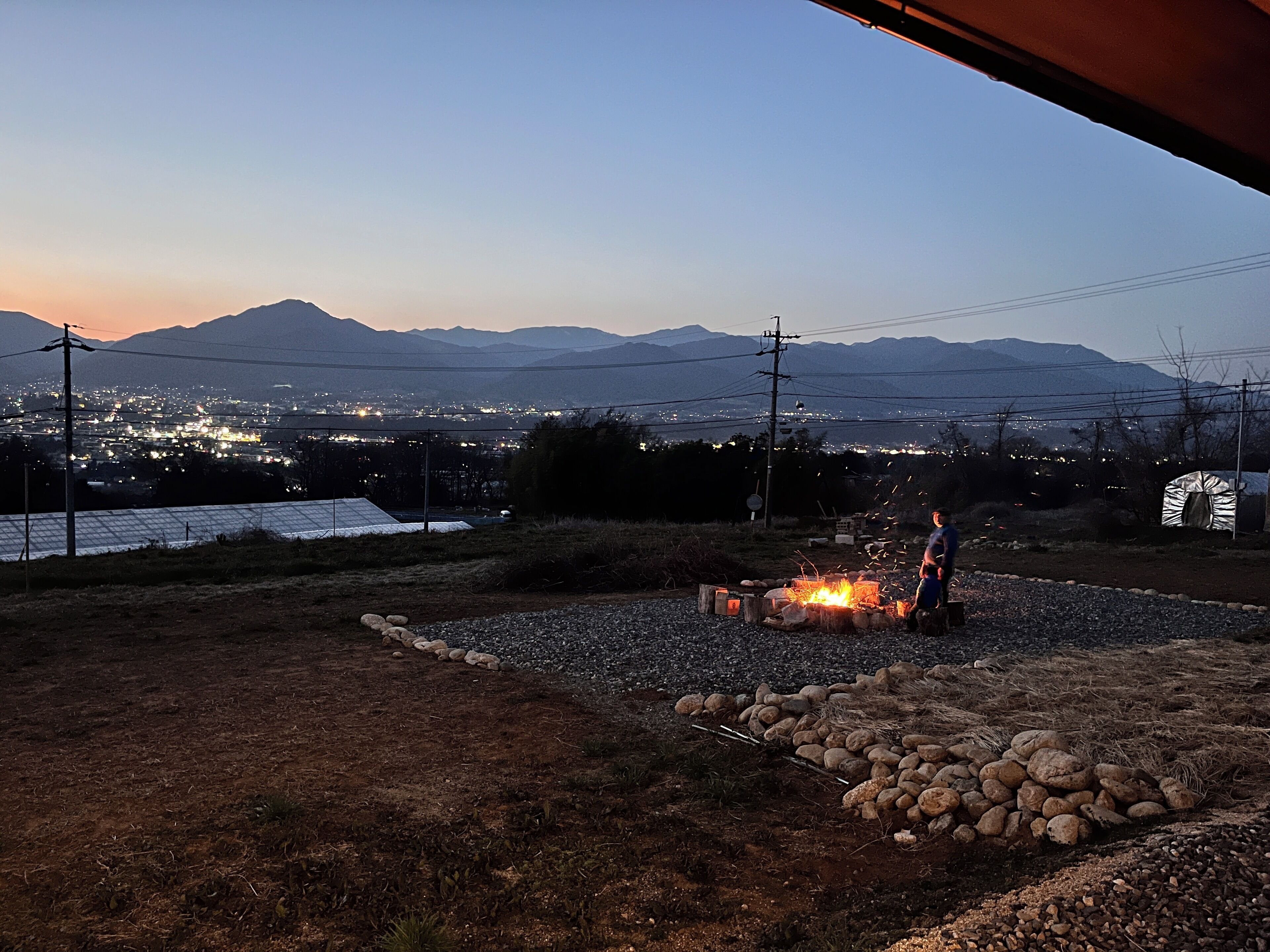 Ein Campingplatz mit Feuerstelle, Zelt und Blick auf eine entfernte Stadt im Abenddämmerung.