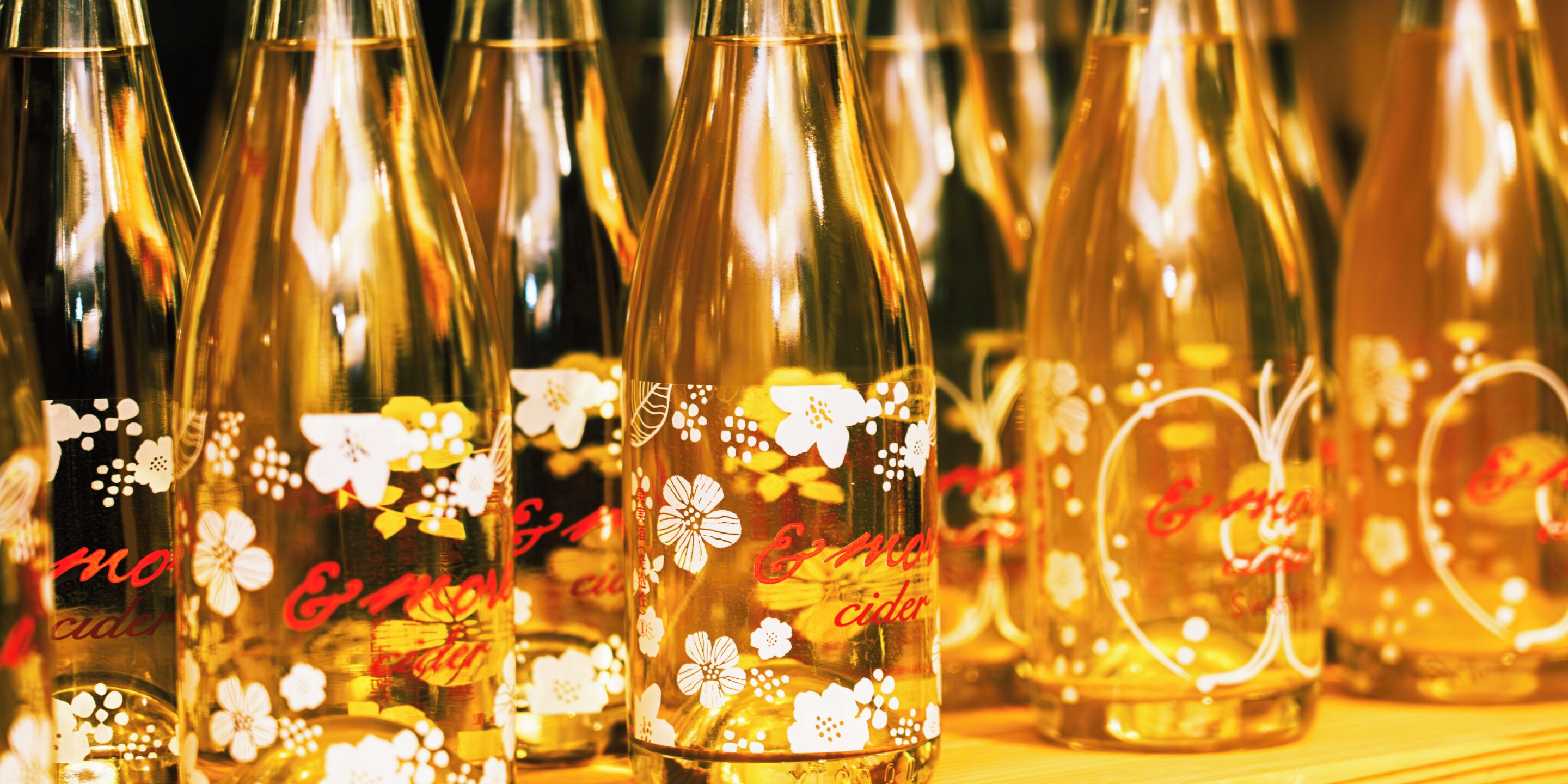 A collection of clear glass bottles with floral designs and the text "C&M Cider" on them.