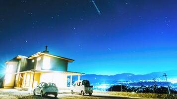 A house with a car parked in front, a truck parked to the side, and a clear night sky with stars.