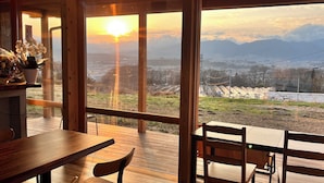 A wooden deck with a table and chairs, overlooking a snowy landscape with mountains and a river. - Cider Barn &more (Iida)