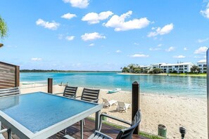 A deck with a table and chairs overlooking a beach and water.