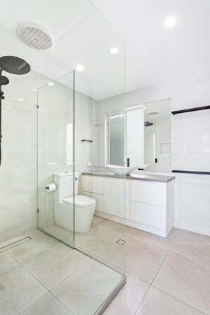 Ein modernes Badezimmer mit einer Duschkabine, einer Toilette und einem Waschbecken mit Spiegel.