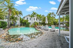 A swimming pool with lounge chairs, surrounded by palm trees and a covered area.