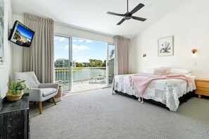 Ein Schlafzimmer mit Bett, Sessel, Fernseher, Deckenventilator und einem Balkon mit Blick.