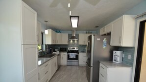A compact kitchen with white cabinets, stainless steel appliances, and a tiled backsplash. - Salty Breeze Canal Front Pool Home W Boat Dock (Palm Coast)