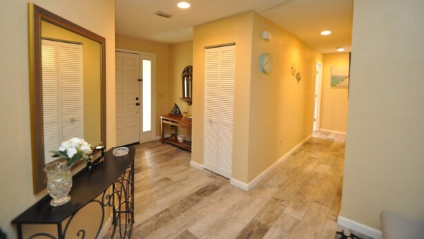 A hallway with a dining area, featuring a table with chairs, a vase with flowers, and a clock on the wall. - Salty Breeze Canal Front Pool Home W Boat Dock (Palm Coast)