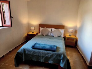 A neatly made bed with a blue blanket and pillows, two bedside lamps, and a framed picture on the wall. - Casita-1 To 2guests-pool-patio-bbq-parking (Huercal-Overa)