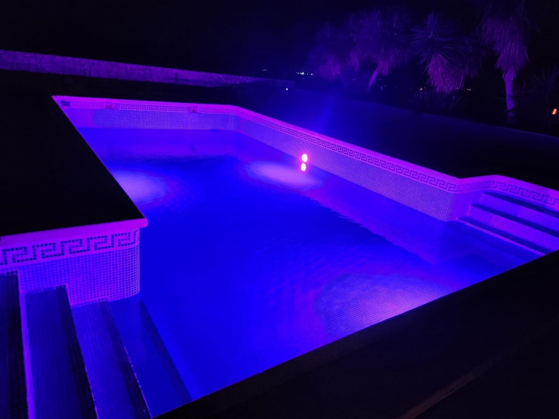 A swimming pool with steps leading into it, surrounded by a dark environment.