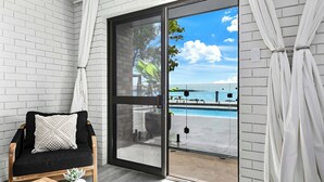 A room with a black sofa, a wooden table, and a view of a swimming pool through a glass door.