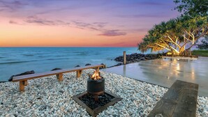 A wooden bench and a fire pit on a pebbled deck by the water.