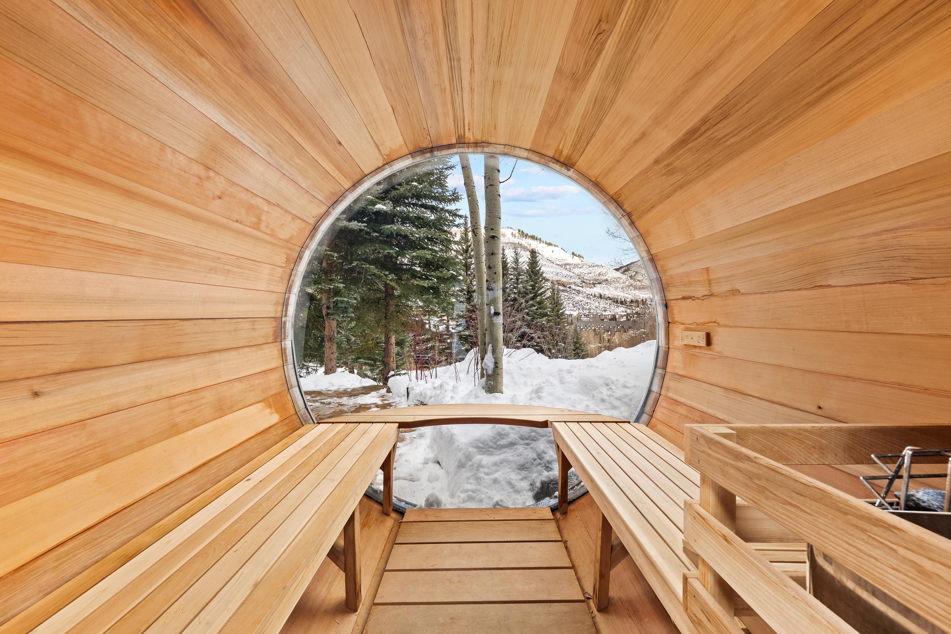 A wooden sauna with benches and a glass window offering a view of a snowy landscape.