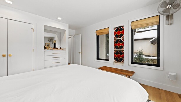 Un dormitorio con una cama grande, un armario, un espejo, una ventana con vistas y un ventilador de pie.