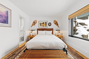 Ein Schlafzimmer mit einem Bett, Nachttischen, einem Fenster mit Blick auf Schnee und einem gerahmten Bild an der Wand.