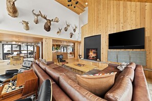 A spacious living room with a fireplace, leather sofas, a chessboard, and mounted animal heads on the wall.