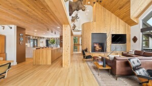 Un amplio salón con chimenea, techo de madera y una cocina moderna al fondo.