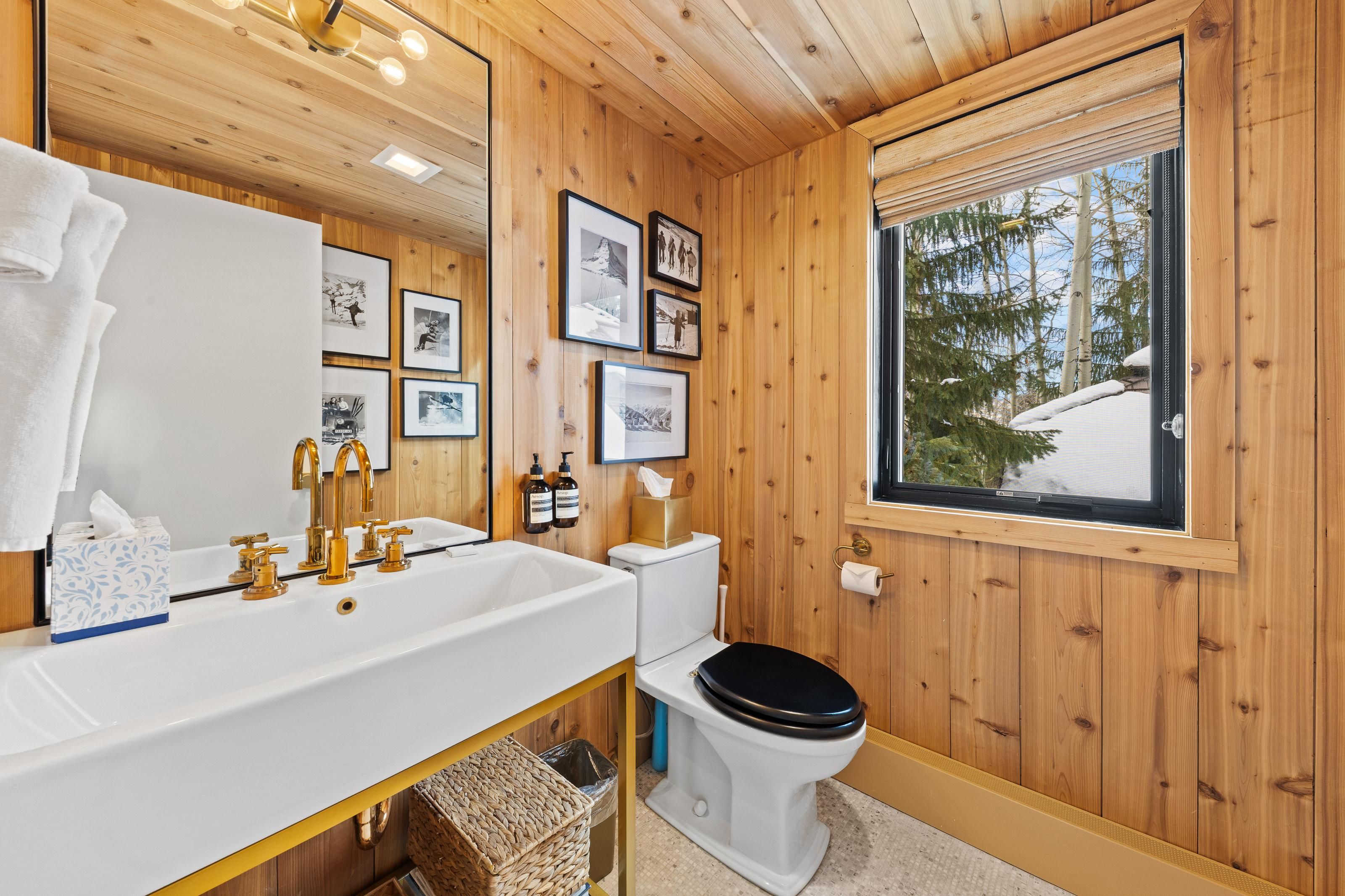 Une salle de bain avec des murs en bois, un lavabo blanc avec des robinets dorés, des toilettes et des tableaux encadrés accrochés au mur.