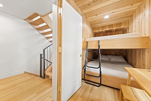 Ein kleines Zimmer mit Etagenbett, Holzboden, einem kleinen Tisch und einer Treppe.