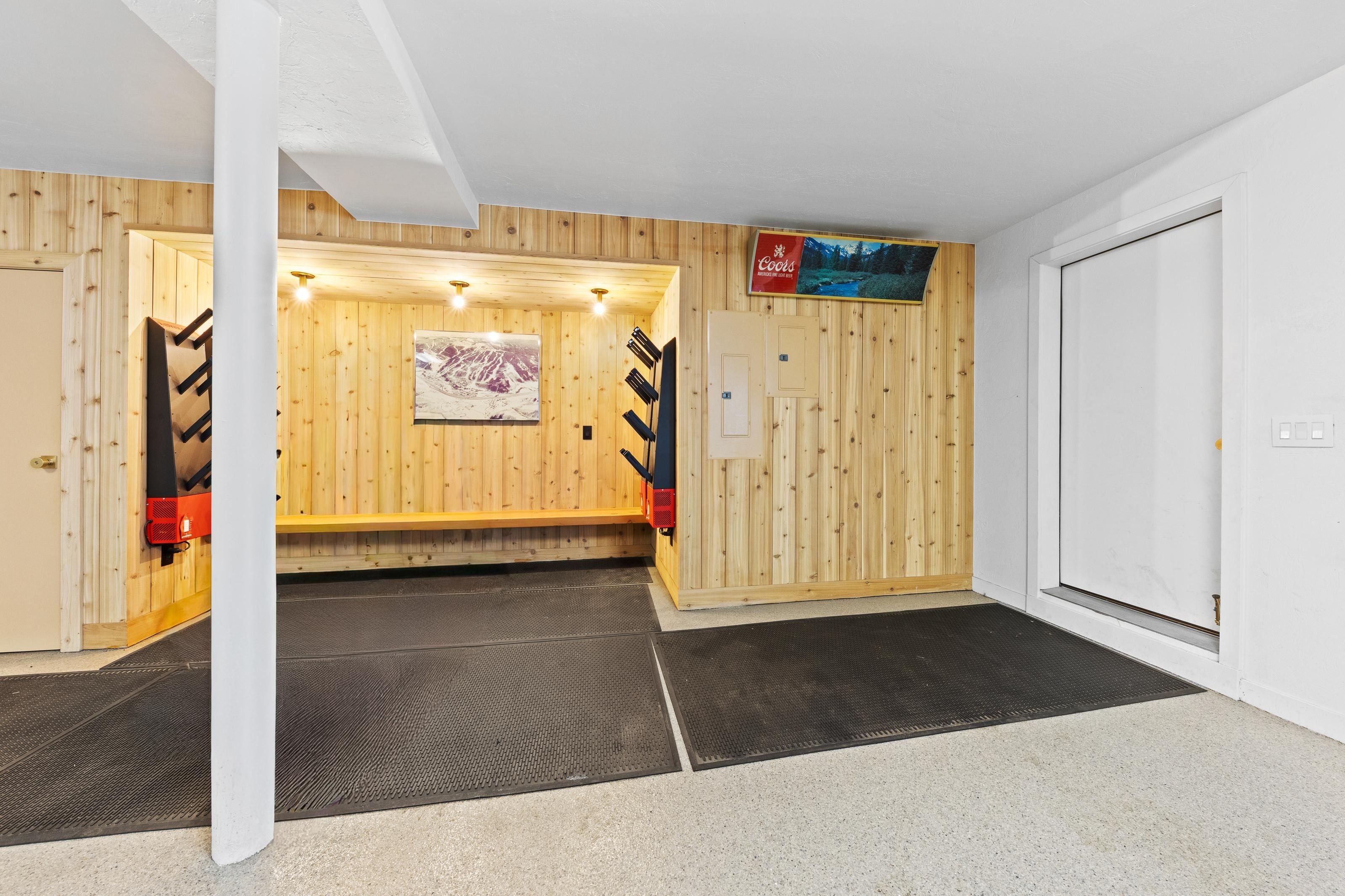 A room with wooden walls, a mounted Coors sign, a door, and a bench.