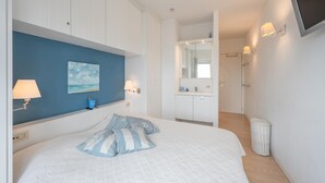 A bedroom with a bed, a blue accent wall, a painting, and a bathroom visible in the background. - Spacious 9-guest Knokke Apt (Knokke-Heist)