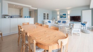 A spacious living area with a wooden dining table and chairs, a white sofa set, and a flat-screen TV mounted on the wall. - Spacious 9-guest Knokke Apt (Knokke-Heist)