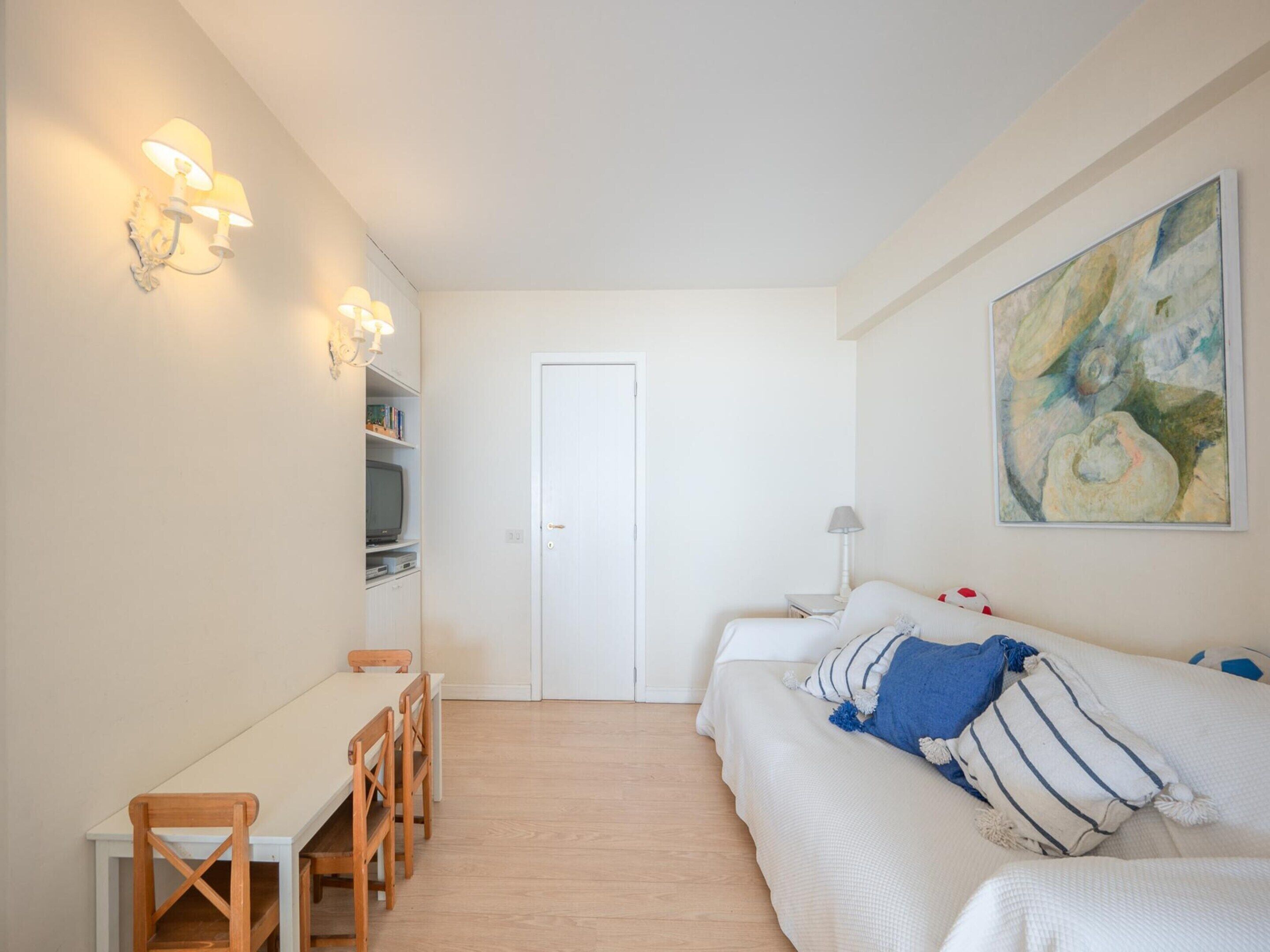 Ein Zimmer mit einem Bett, einem Schreibtisch und einem Stuhl. Eine Tür befindet sich in der Mitte, und ein Bild hängt an der Wand.