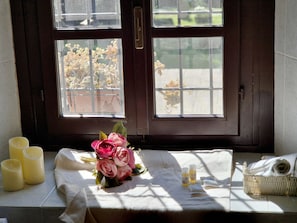 Una ventana con vista a un jardín, un ramo de flores y velas sobre una mesa.