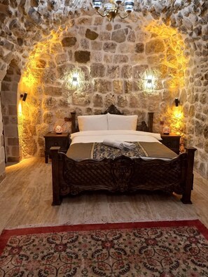 A stone-walled bedroom with a bed, two nightstands, and a chandelier. - Hakanbey Konağı (Mardin)